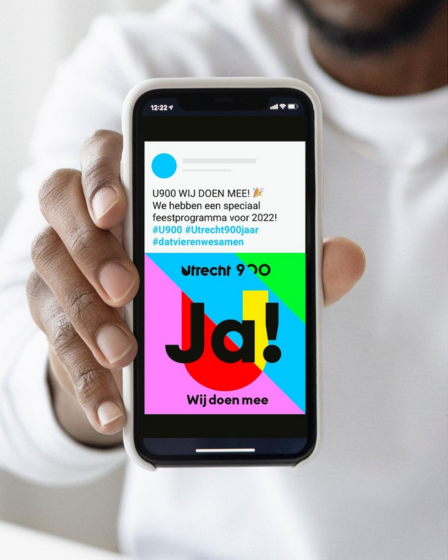 Iemand die een telefoon vast houdt met op het scherm een post van Utrecht 900 jaar.
